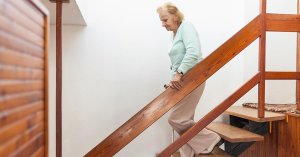 Alte Dame geht eine Holztreppe in ihrem Einfamilienhaus herunter.