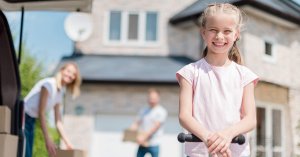 Ein Mädchen vor einem Haus, im Hintergrund die Eltern - Immobilienverkauf